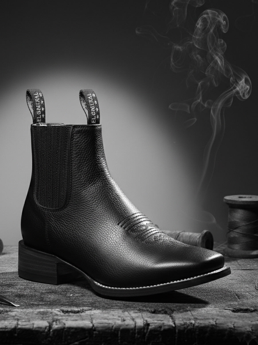 Black leather Chelsea boot on a wooden surface with a dark background