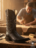 Atelier No. 54 men’s western boot in black lizard leather on an artisan workbench, showing fine scale texture, tonal embroidery, and handcrafted structure.

