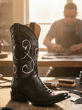 The First Atelier Atelier No. 58 “El Meridiano” men’s western boot in black ostrich leather on an artisan workbench, highlighting natural quill texture, tonal embroidery, and hand-finished construction.
