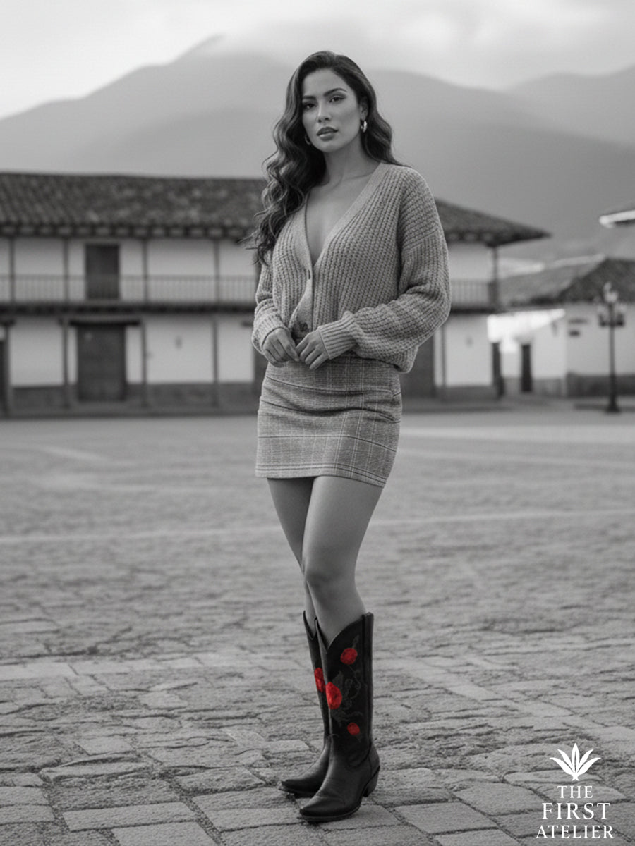 Black-and-white portrait of a woman in a soft knit dress wearing the La Rosa del Silencio Boot on a tranquil plaza at dusk — poised simplicity.