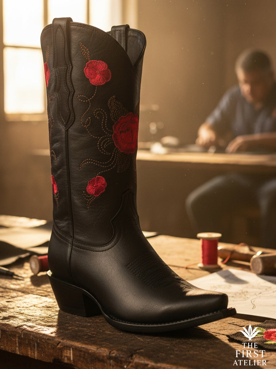 The La Rosa del Silencio Boot — handcrafted black leather boot with crimson floral embroidery and rose-red threadwork on the artisan’s bench in León.