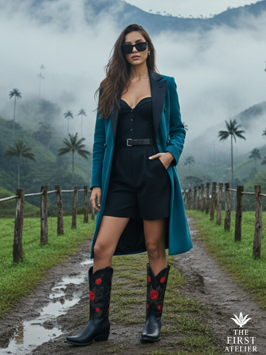 The La Rosa del Silencio Boot worn with a teal coat and black dress on a misty highland road — grace and resolve framed by mountain air.
