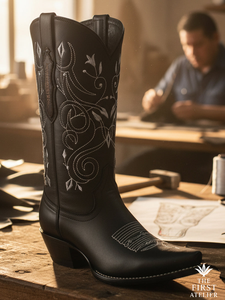 The La Flor del Egeo Boot — hand-crafted black leather boot with silver vine embroidery, resting on the artisan’s bench in León.