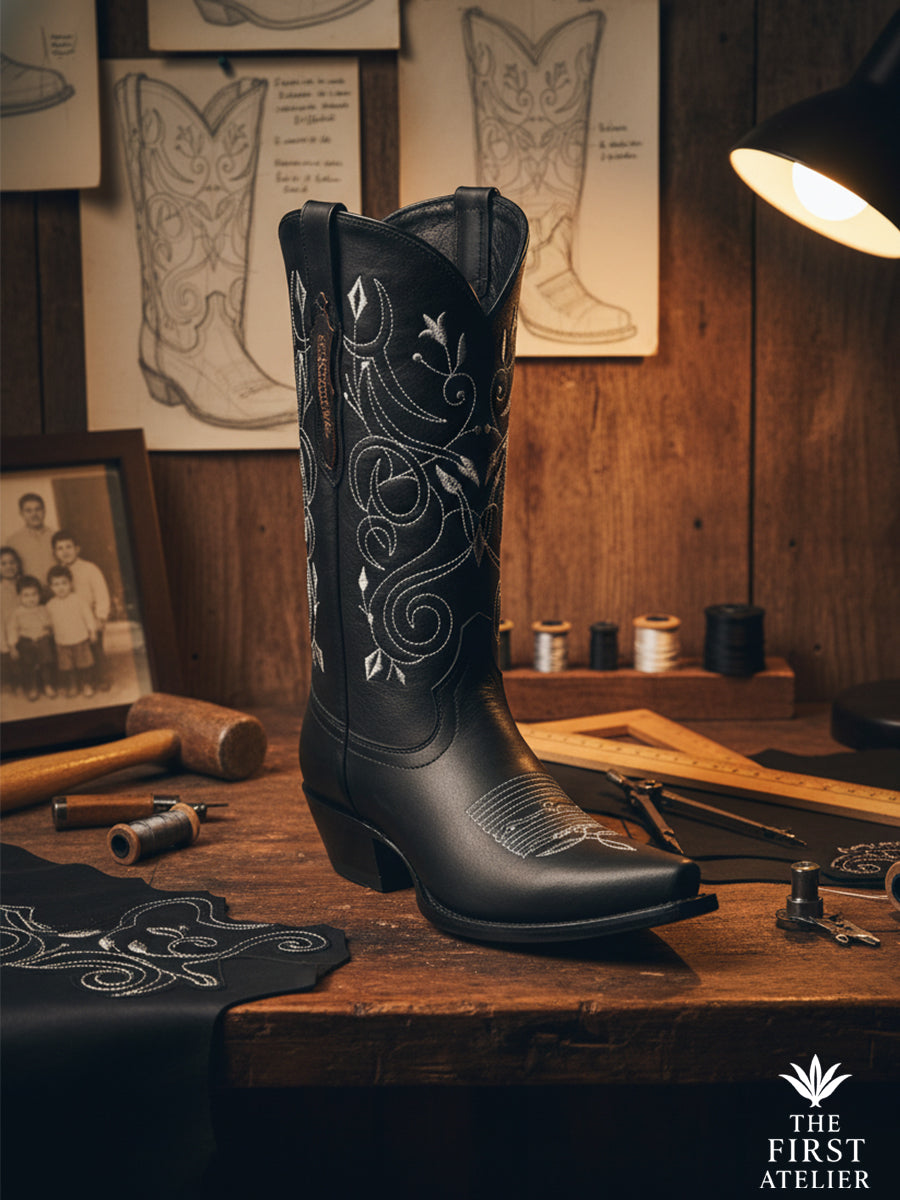 Close-up of the La Flor del Egeo Boot in the artisan’s workshop — sketches, leather, and soft lamplight reflecting the craft’s devotion.