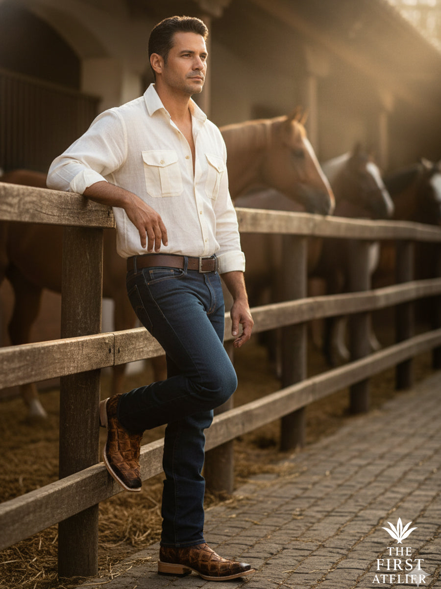 Man leaning against a wooden stable fence wearing a men’s western boot crafted in ochre pirarucu leather, set within a calm rural environment that reflects craftsmanship, balance, and grounded presence, The First Atelier, Atelier No. 34.
