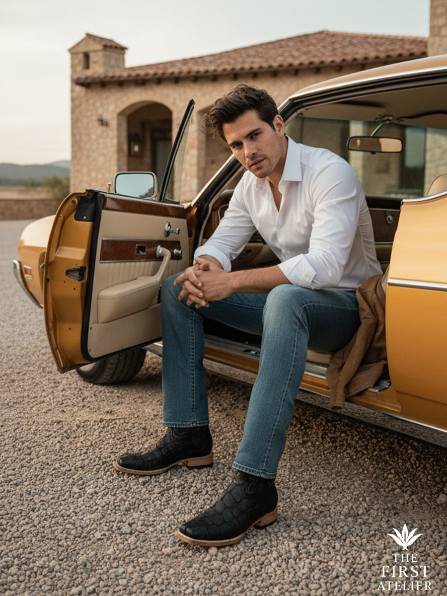 Man seated in a classic automobile wearing the El Tránsito Boot in black pirarucu (monster fish) leather, captured in a moment of pause between journeys, blending refined tailoring with modern western movement, The First Atelier, Atelier No. 36.
