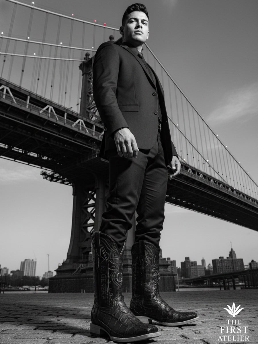 Black-and-white editorial portrait of a man standing beneath an urban bridge wearing the El Tránsito Boot in black pirarucu (monster fish) leather, expressing movement, tension, and modern western masculinity in transit, The First Atelier, Atelier No. 36.
