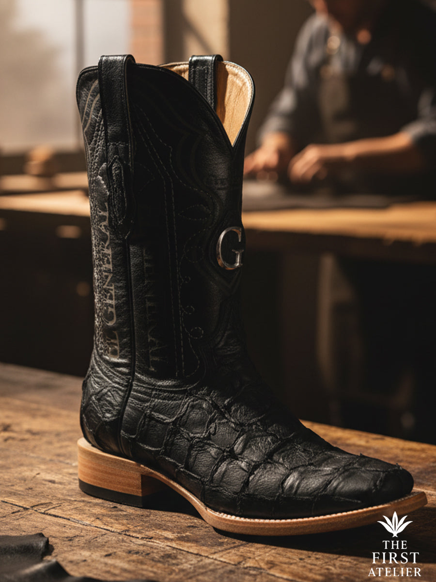 The El Tránsito Boot — men’s western boot crafted in black pirarucu (monster fish) leather, photographed on an artisan’s worktable, showcasing natural scale texture and disciplined western construction, The First Atelier, Atelier No. 36.
