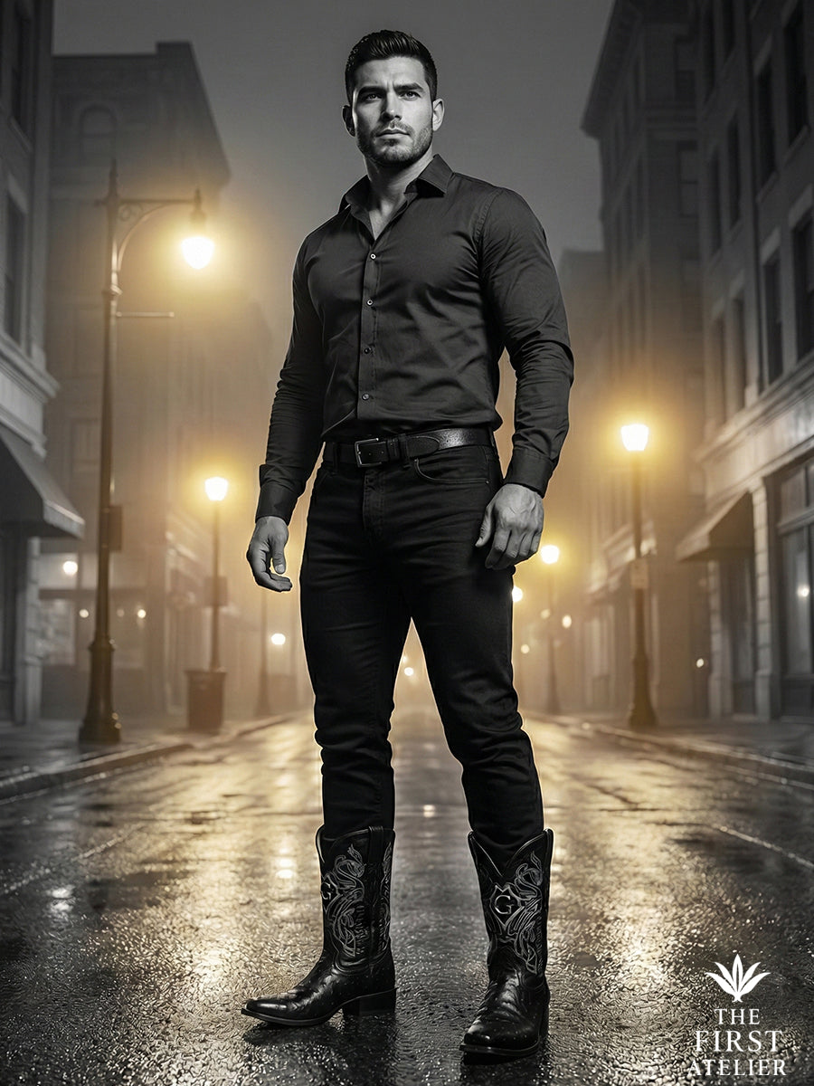 Black-and-white portrait of a man standing on a city street at night wearing The First Atelier Atelier No. 47 men’s western boots in black ostrich leather — sharp silhouette, controlled strength, and modern authority.

