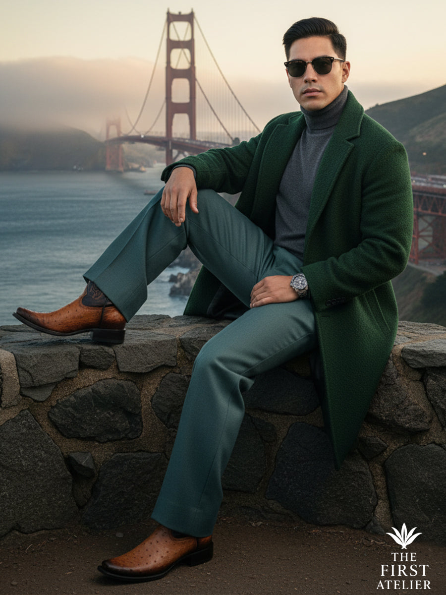 Man seated by the coast wearing The First Atelier Atelier No. 48 men’s western boots in cognac ostrich leather — refined travel style, warm leather tones against sea and architecture, effortless authority.
