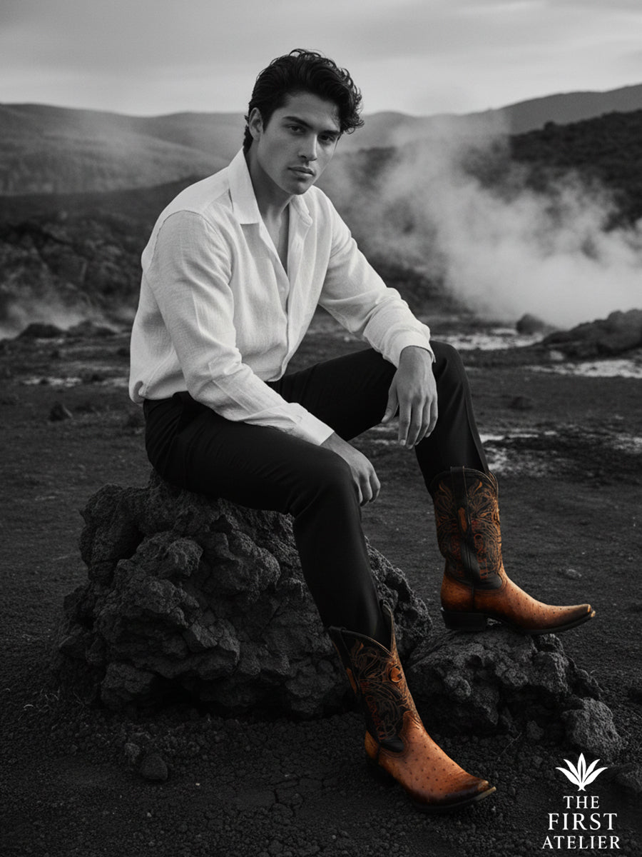 Black-and-white image of a man seated on rock formations wearing The First Atelier Atelier No. 48 men’s western boots in cognac ostrich leather — strong silhouette, natural posture, and quiet endurance beyond color.
