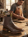 Close-up of Atelier No. 68 El Trazo Maestro Boot in rich tobacco leather on a workshop table, surrounded by artisan tools and sketches
