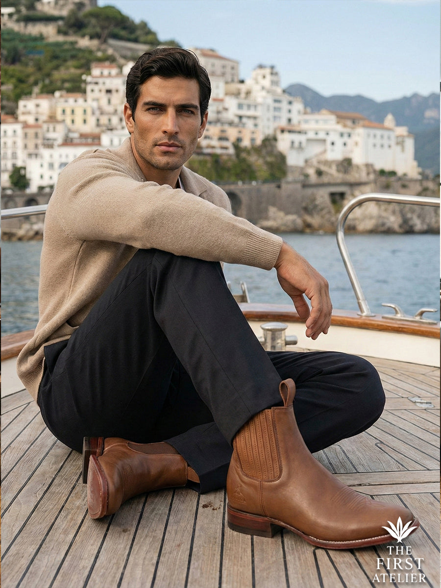 Man sitting on the deck of a classic wooden boat wearing Atelier No. 75 El Rumbo Boot, embodying relaxed coastal elegance.