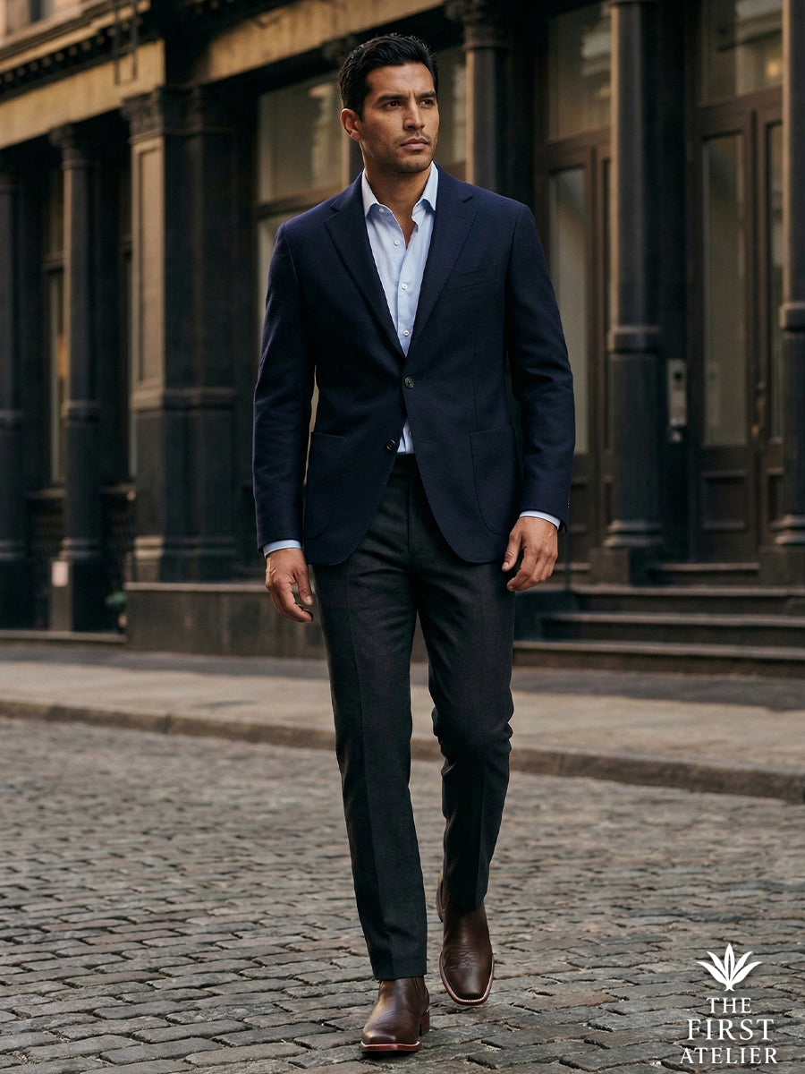Formal city style: Man in a navy suit walking on cobblestones wearing the dark brown Atelier No. 76 El Puente Chelsea boot.