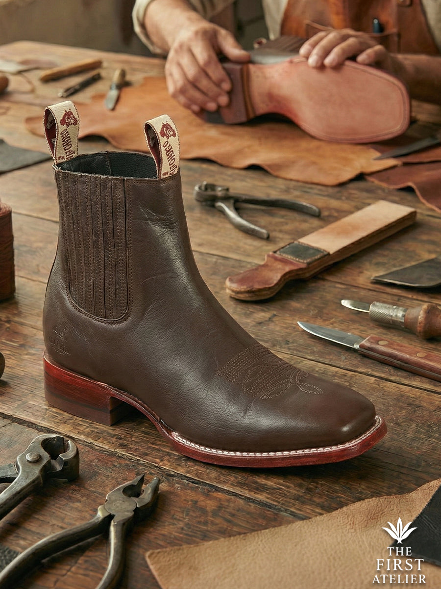Artisan detailing the Atelier No. 76 El Puente Boot in dark espresso full-grain leather, featuring a contrasting cherry-finish stacked heel.