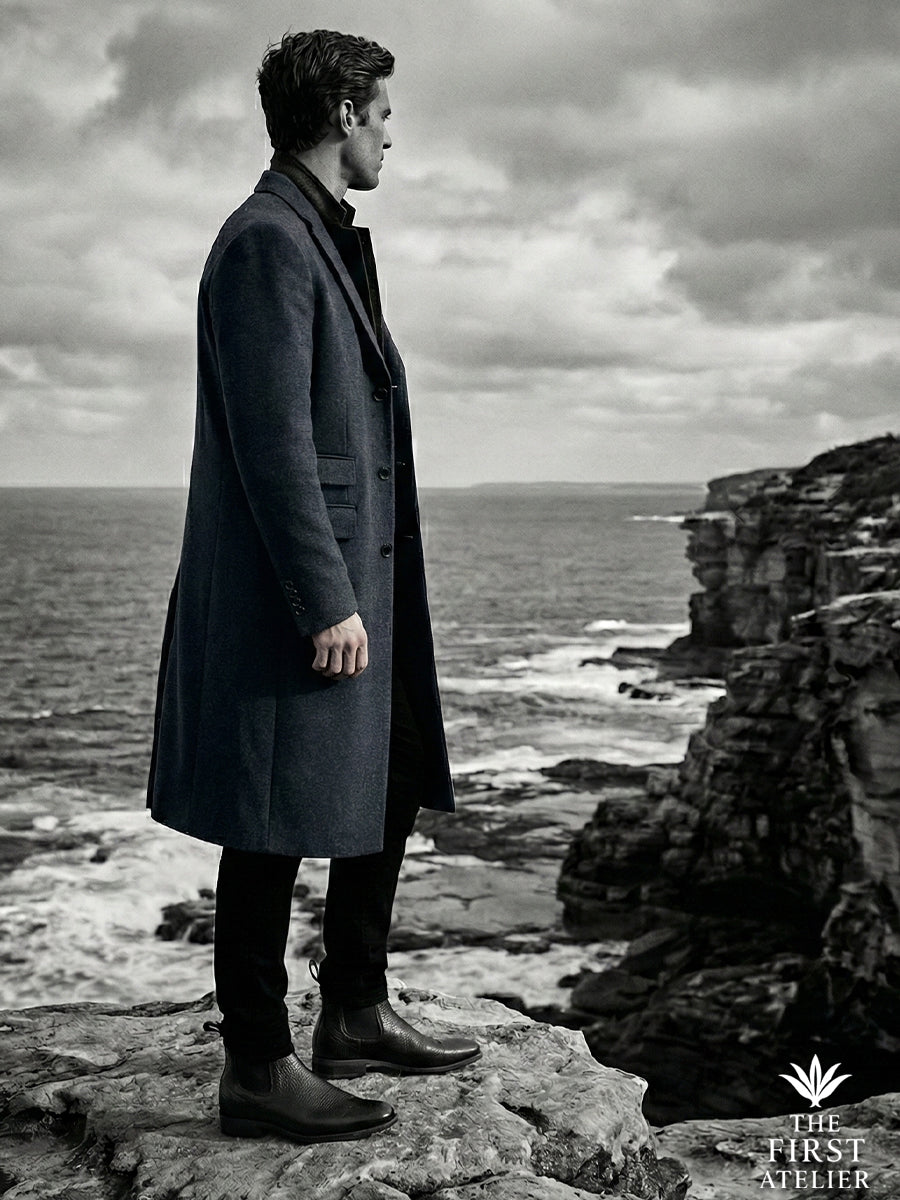 Dramatic black and white shot of a man standing guard on a coastal cliff, embodying the stoic spirit of the El Centinela boot.