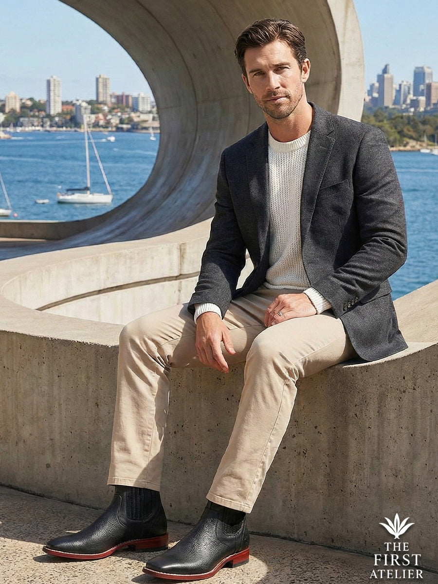 Gentleman sitting on a concrete seawall with a city bay background, wearing the versatile black textured Atelier No. 79 boot.