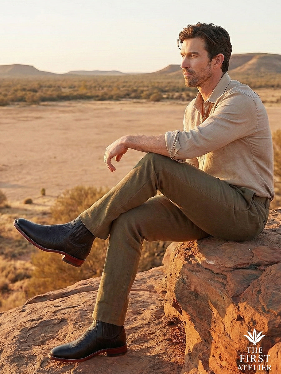 Man sitting on red rocks in a desert landscape wearing Atelier No. 79, showing the boot's durability and adaptability.