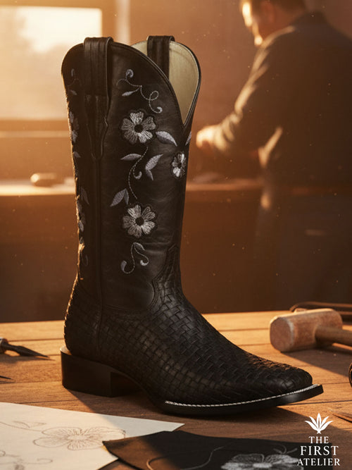 Close-up of Atelier No. 11 La Rosa de Plata boot, featuring hand-woven black leather vamp and sterling silver floral embroidery on a craftsman workbench.