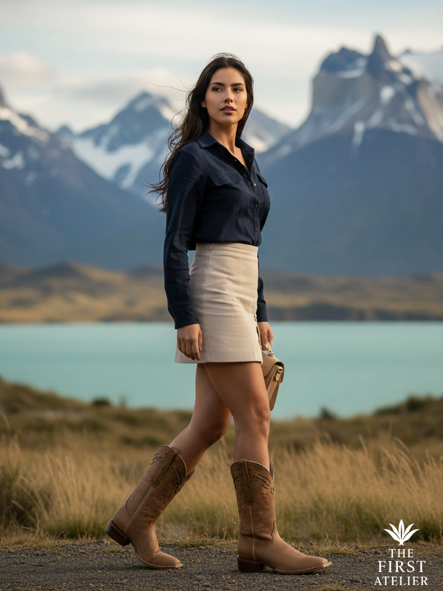 Editorial field portrait with mountains — wool skirt, navy shirt, and La Rosa del Altiplano Boot in golden grass, Atelier No. 26.