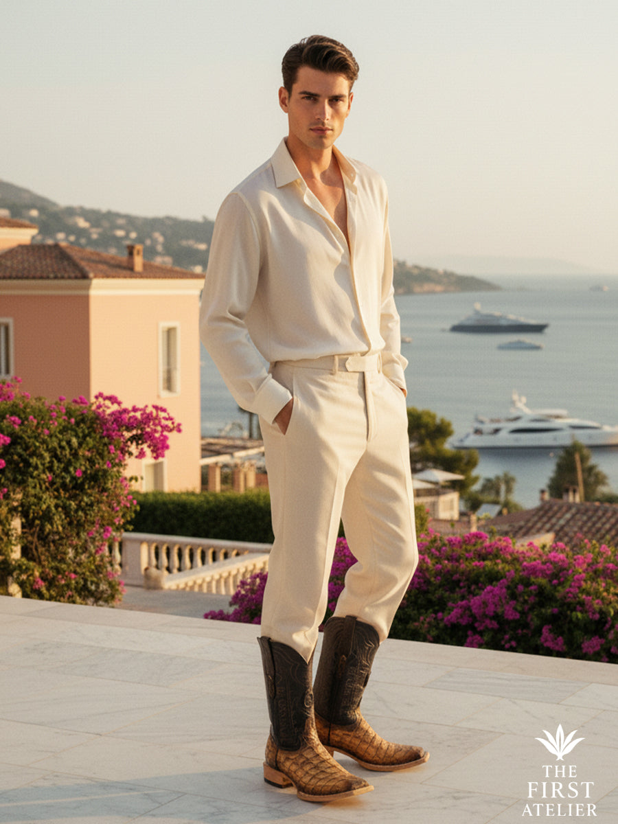 Man standing on a coastal terrace wearing the El Umbral Boot in textured brown leather, styled with relaxed tailoring and overlooking the sea, expressing a refined western presence, Atelier No. 33.
