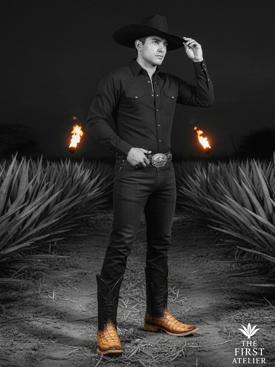 Black-and-white editorial portrait of a man wearing the El Umbral Boot in textured brown leather, styled with a hat and dark attire, expressing a strong western presence at night, Atelier No. 33.

