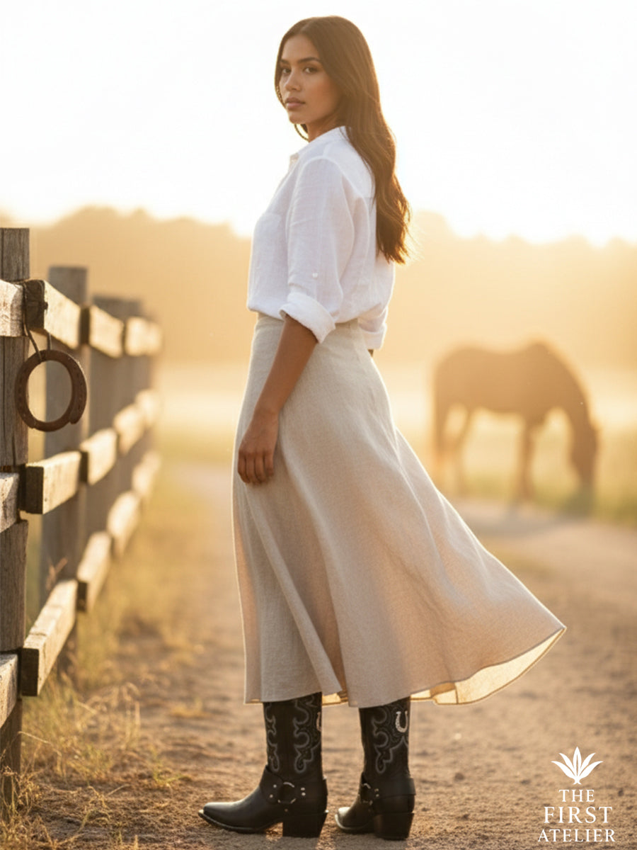 Woman at sunrise by a horse corral wearing La Dama Nocturna Boot — black leather cowboy boots with silver stitchwork and modern attitude, Atelier No. 9.