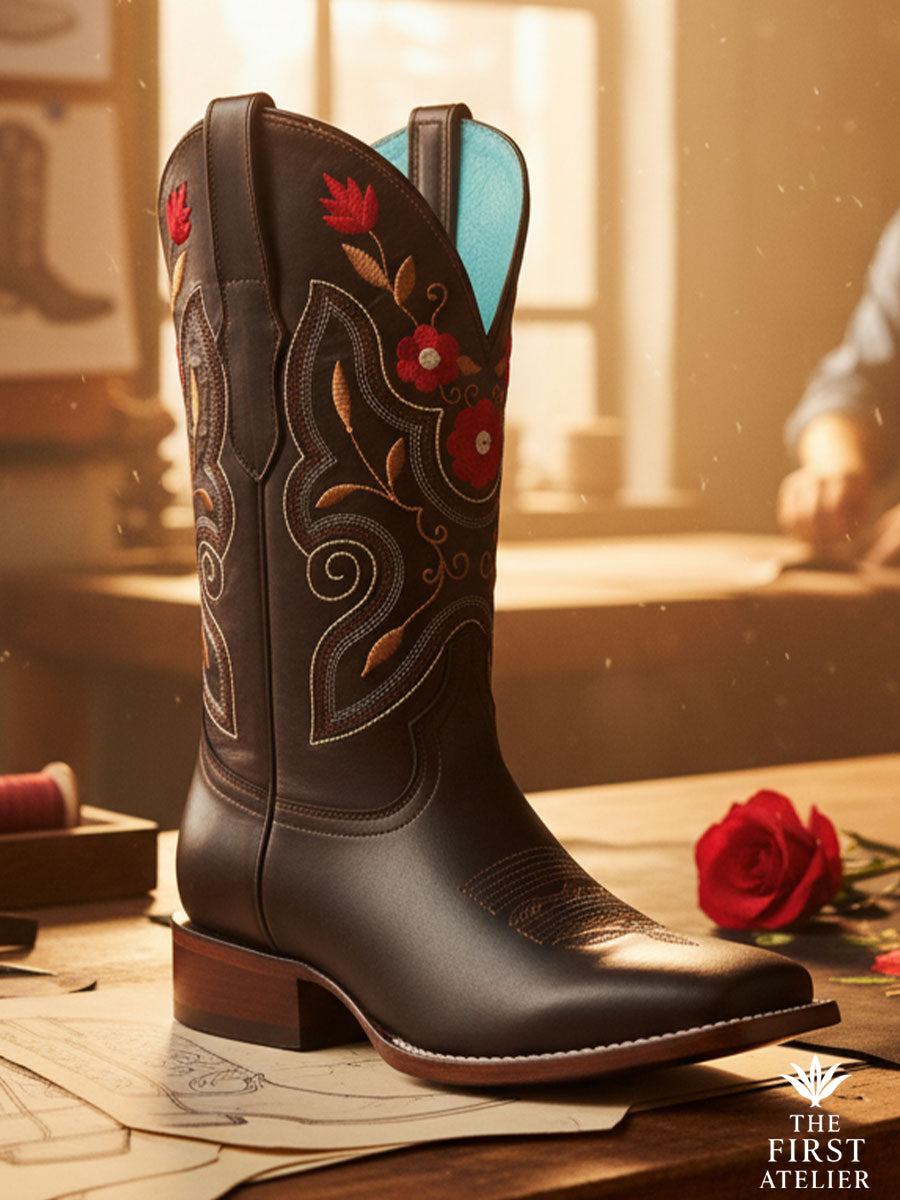 Close-up of La Flor de Fuego Boot — espresso leather with red and gold floral embroidery and elegant western stitching, resting beside a single red rose, Atelier No. 02.