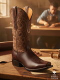 Close-up of the La Flor del Camino Boot in rich brown leather with hand-tooled floral carving, handcrafted in León, Guanajuato, displayed on an artisan workbench, Atelier No. 12.
