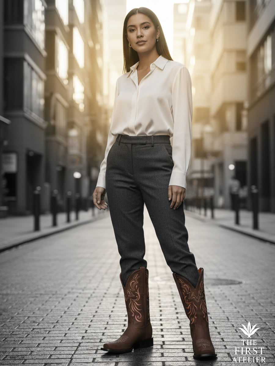 City daylight portrait of a woman in a crisp white blouse and slate trousers wearing La Rosa del Atardecer Boot — heritage western silhouette styled with modern urban ease, Atelier No. 14