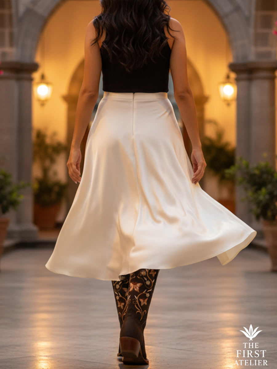 Rear view of a woman twirling under soft archway light in a white skirt, wearing La Mariposa Nocturna Boot — graceful and bold, Atelier No. 6.

